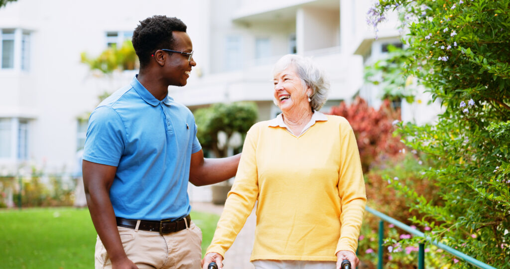 A senior woman with a walker and a tour guide walk through a senior living campus