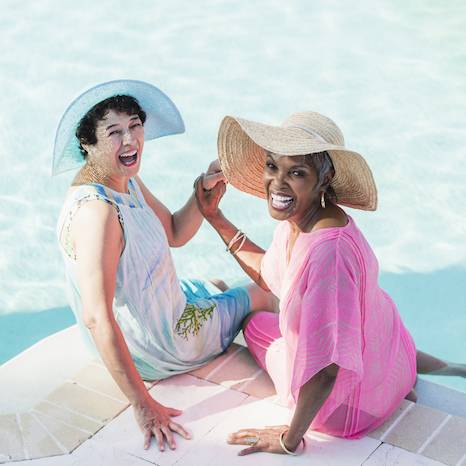 Two senior women sitting on pool deck, feet in water